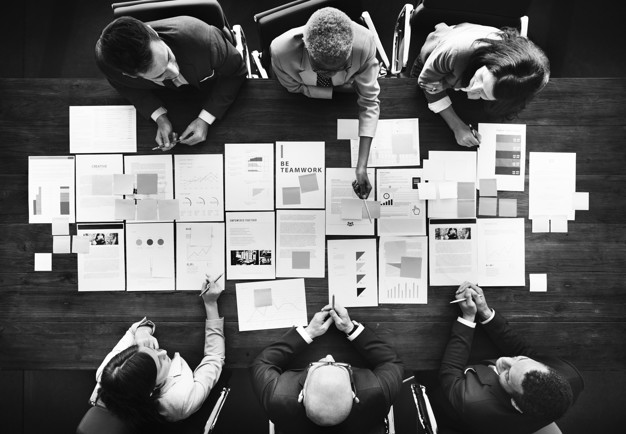 Sex personer sitter vid ett bord och analyserar sidor tillhörande en företagspresentation